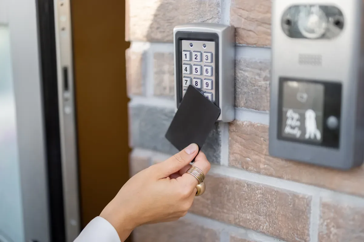 Person holding a black RFID card to a keypad reader beside a brick wall