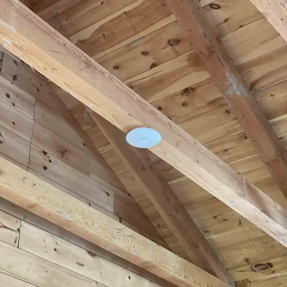 Wi-Fi access point mounted on a wooden ceiling beam in a cabin