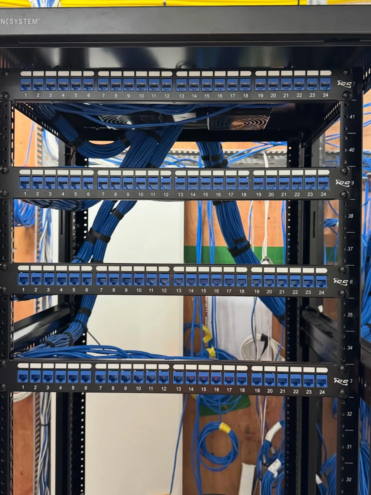 Open network rack with patch panels being populated with blue cabling