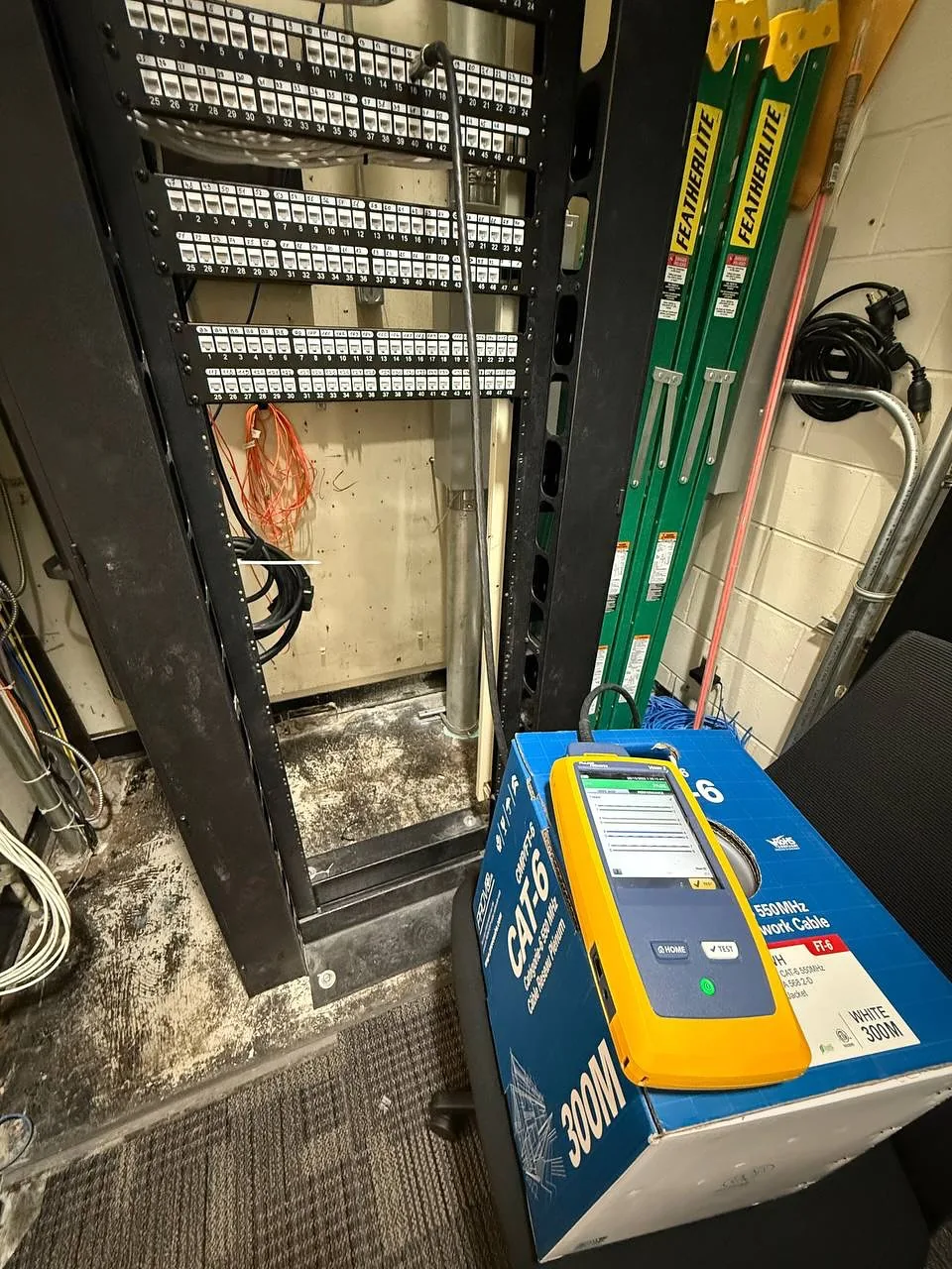 Network rack with patch panels and a Fluke tester on the floor
