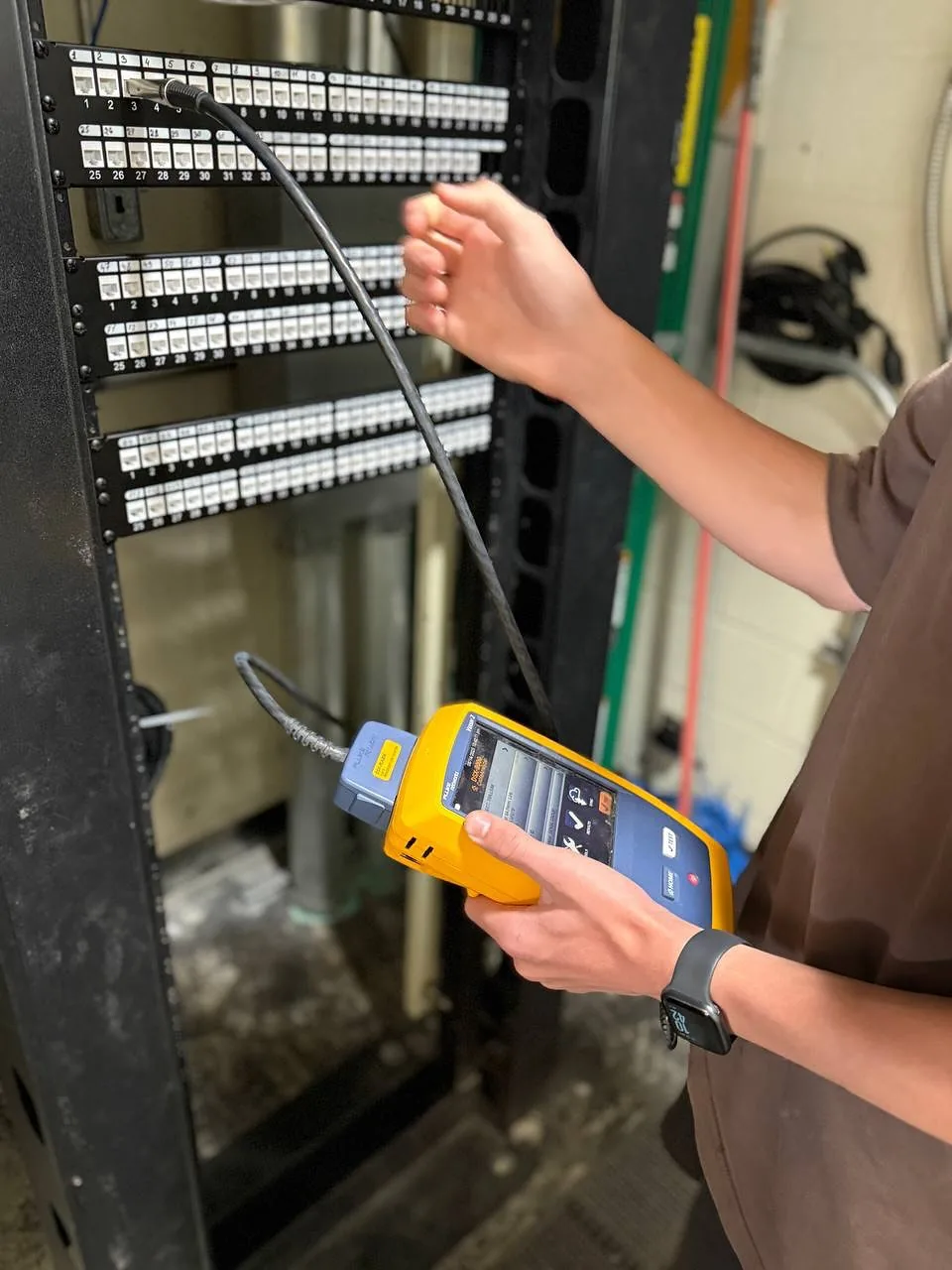 Technician plugging a Fluke tester into a patch panel port