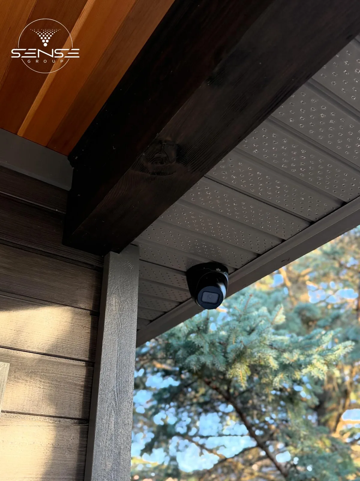 UNV turret camera installed under a wood soffit beside a spruce tree