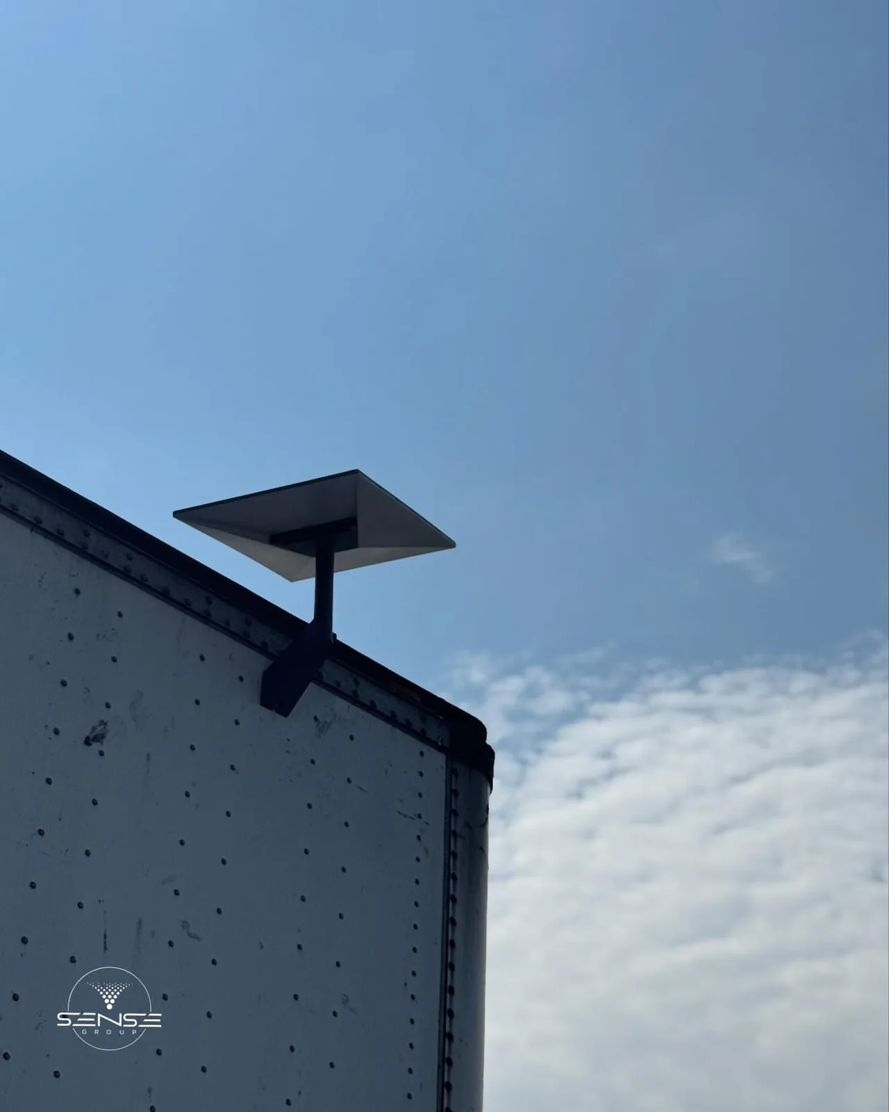 Starlink dish on the corner of a dark roof against a blue sky