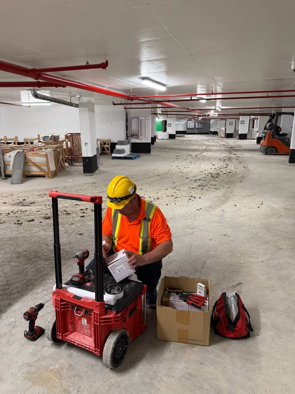 Technician checking a plan beside a tool cart in a parking garage