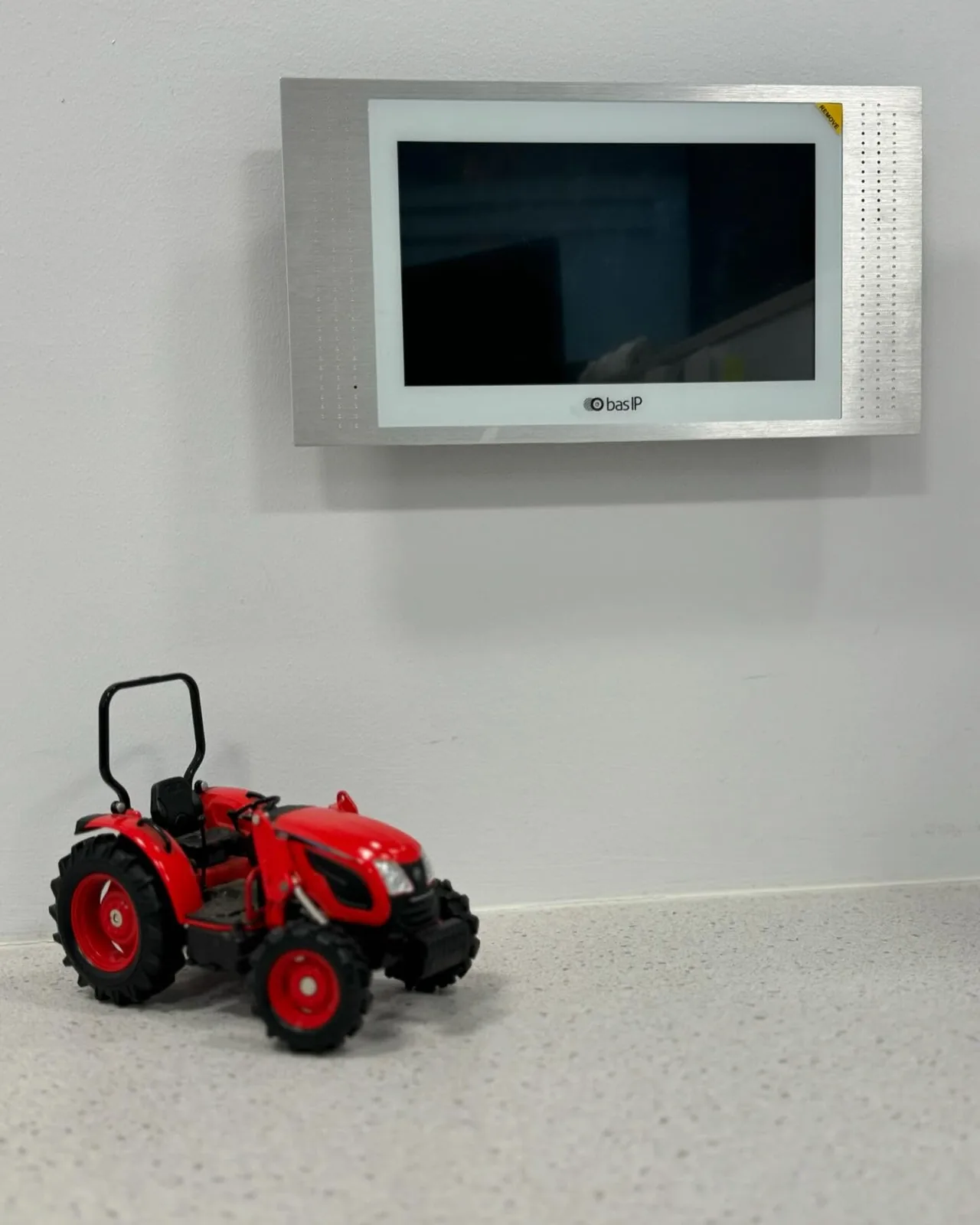 BAS-IP indoor intercom monitor on a wall with a red toy tractor below