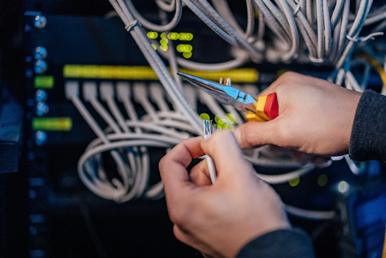 Hands punching down cables in a panel with a red tool
