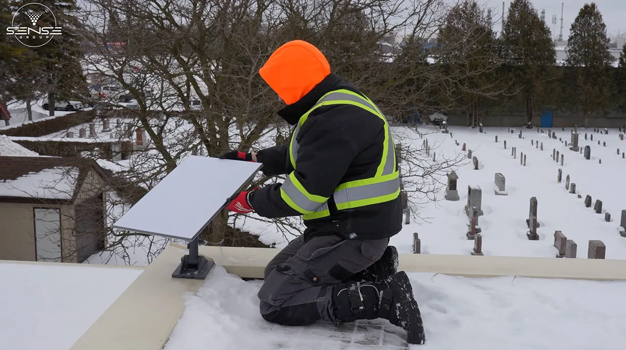 Installer in a high-visibility jacket mounting a Starlink dish on a snowy church roof