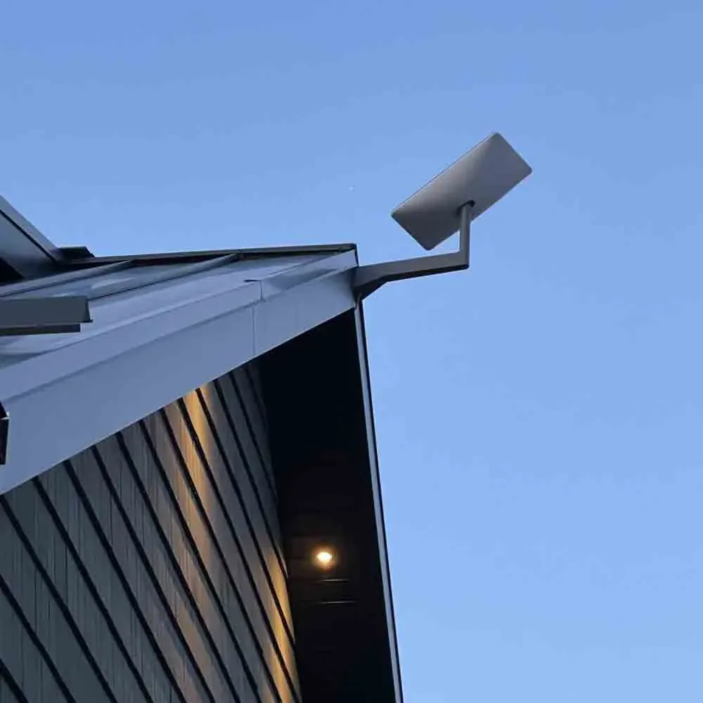 Starlink dish mounted on the edge of a dark modern roof against a blue sky
