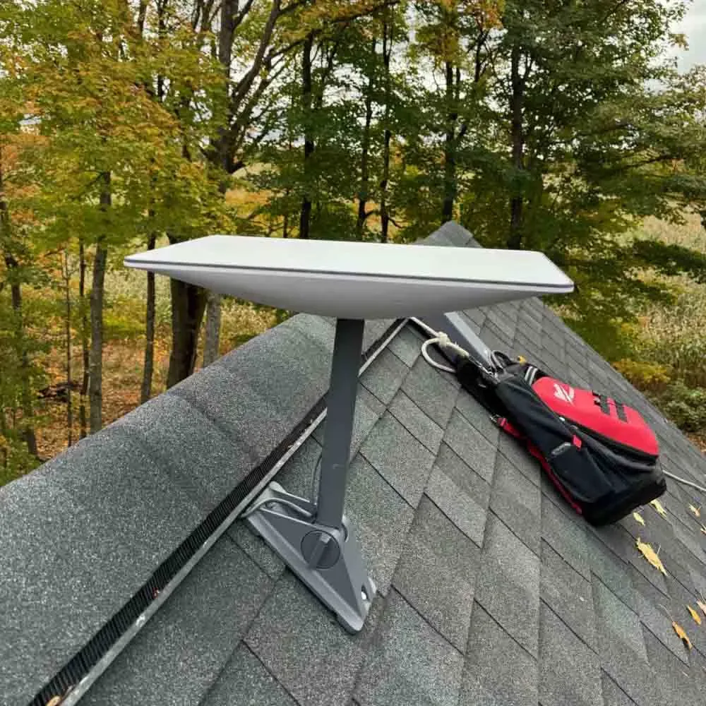 Starlink dish on a shingle roof in autumn with a tool bag beside it