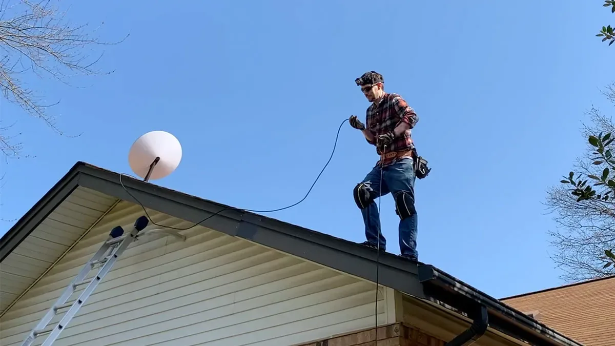 Technician standing on a house roof installing a Starlink dish