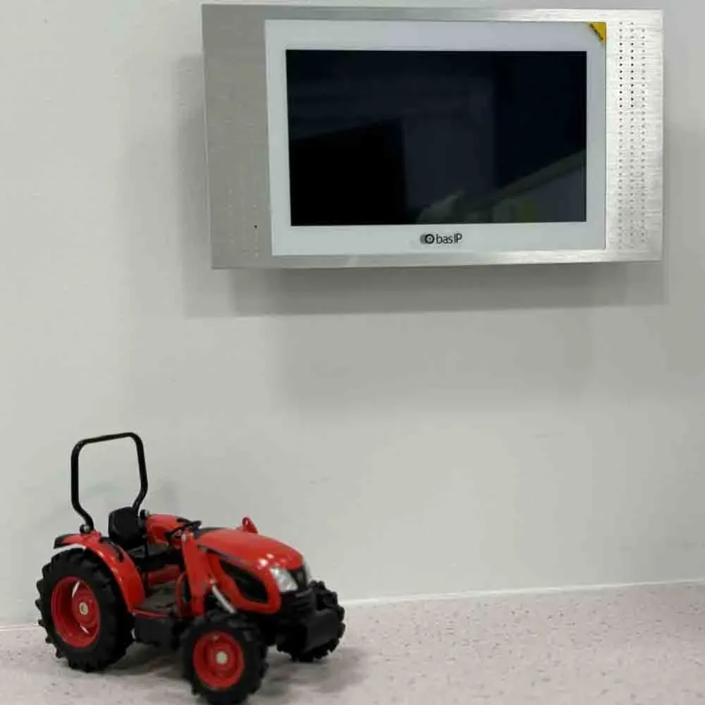BAS-IP indoor intercom monitor on a white wall with a red toy tractor on the floor