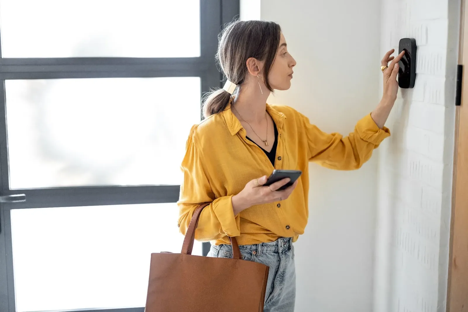 Woman using a touch access panel at a building entrance while holding a phone
