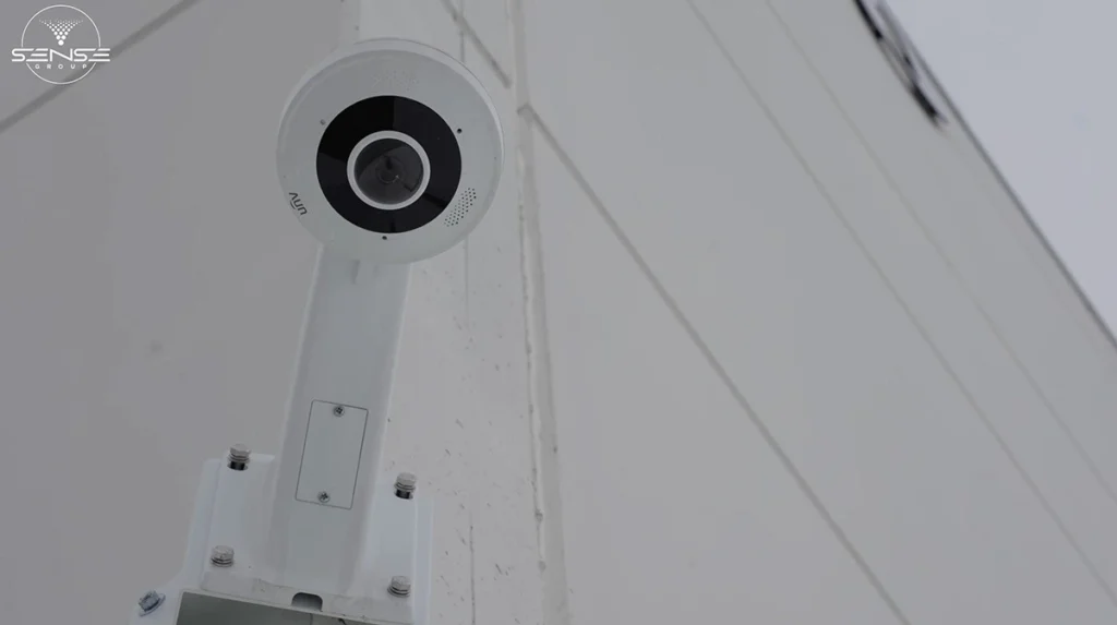 White fisheye CCTV security camera installed on an exterior wall bracket, providing wide-angle video surveillance coverage for building perimeter monitoring.
